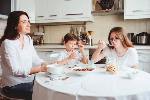 Happy family having breakfast at home. Mother with two kids eating in modern white kitchen — Stock Photo, Image