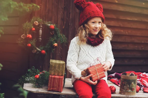 Mutlu çocuk kız kırmızı şapka ve Noel hediyeleri rahat kır evinde kaydırma eşarp yeni yıl ve Noel için dekore edilmiştir. Çocuklarla tatil için hazırlıklar. — Stok fotoğraf