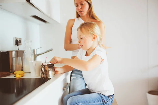 Mãe tomando café da manhã com filha criança em casa na cozinha branca moderna, estilo de vida acolhedor pela manhã — Fotografia de Stock