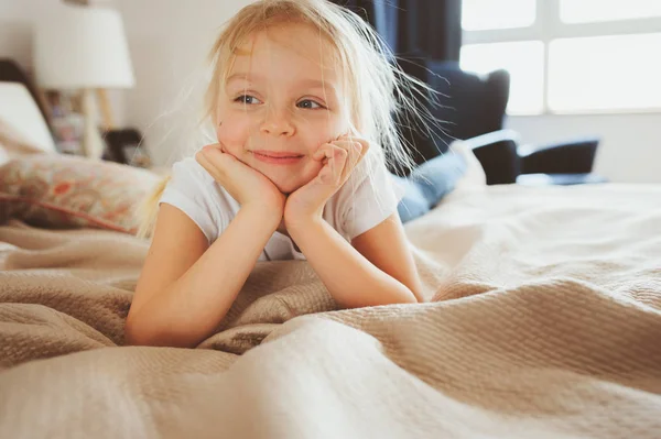Aranyos boldog kisgyermek lány pizsama ágy ül. Gyermek játszik otthon, alkalmi életmód elfog. — Stock Fotó