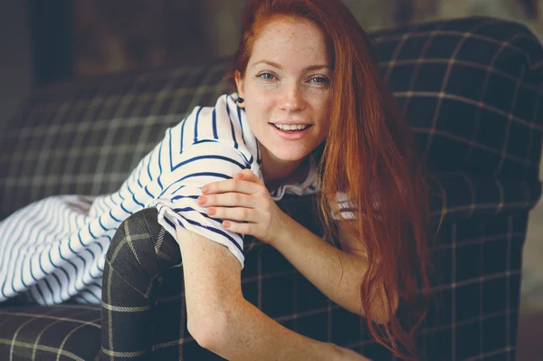 portrait of young beautiful redhead woman relaxing at home in the autumn ot winter cozy evening on couch