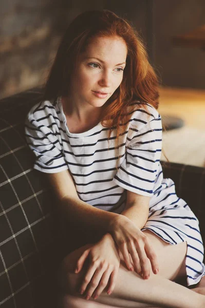 portrait of young beautiful redhead woman relaxing at home in the autumn or winter cozy evening on couch