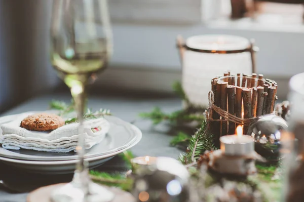 Cenário festivo de mesa de Natal e Ano Novo em estilo escandinavo com detalhes artesanais rústicos em tons naturais e brancos. Lugar de jantar decorado com cones de pinho, ramos e velas — Fotografia de Stock