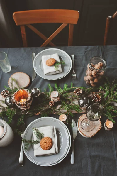 Cenário festivo de mesa de Natal e Ano Novo em estilo escandinavo com detalhes artesanais rústicos em tons naturais e brancos. Lugar de jantar decorado com cones de pinho, ramos e velas — Fotografia de Stock