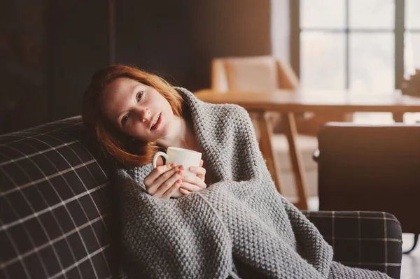 Mujer joven enferma curación con bebida caliente en casa en sofá acogedor, envuelto en manta de punto — Foto de Stock