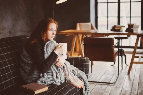 Wanita muda sakit penyembuhan dengan minuman panas di rumah di sofa nyaman, dibungkus dengan selimut rajutan — Stok Foto