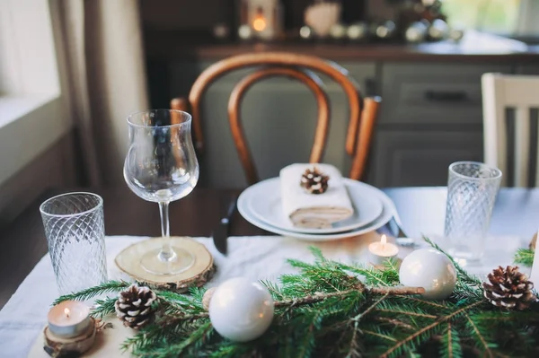 Cenário festivo de mesa de Natal e Ano Novo em estilo escandinavo com detalhes artesanais rústicos em tons naturais e brancos. Lugar de jantar decorado com cones de pinho, ramos e velas — Fotografia de Stock