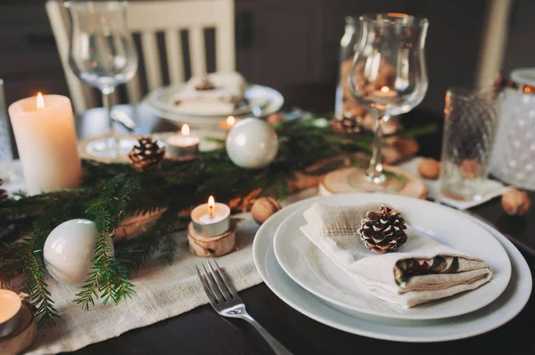 Tovaglia natalizia e Capodanno in stile scandinavo con dettagli rustici fatti a mano in toni naturali e bianchi. Sala da pranzo decorata con pigne, rami e candele — Foto Stock