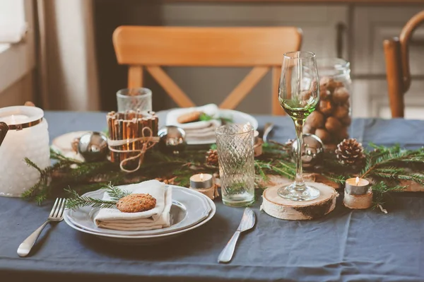 Cenário festivo de mesa de Natal e Ano Novo em estilo escandinavo com detalhes artesanais rústicos em tons naturais e brancos. Lugar de jantar decorado com cones de pinho, ramos e velas — Fotografia de Stock