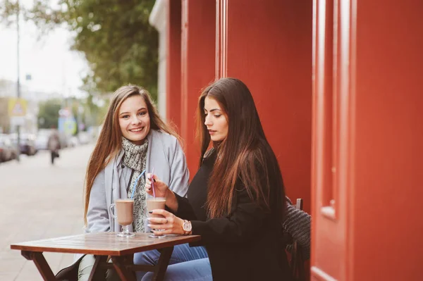 Due amiche felici che parlano e bevono caffè nella città autunnale nel caffè. Incontro di buoni amici, studenti alla moda giovani con trucco naturale . — Foto Stock