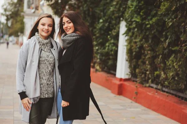 Twee jonge gelukkig vriendinnen wandelen op de straten van de stad in casual mode outfits, het dragen van warme jassen en plezier — Stockfoto