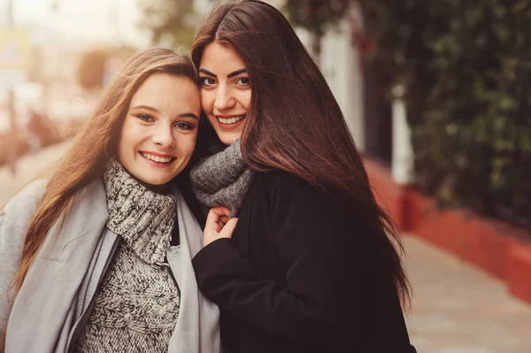 Дві молоді щасливі подружки, що ходять по міських вулицях в повсякденному одязі, одягнені в теплі пальто і розважаються — стокове фото