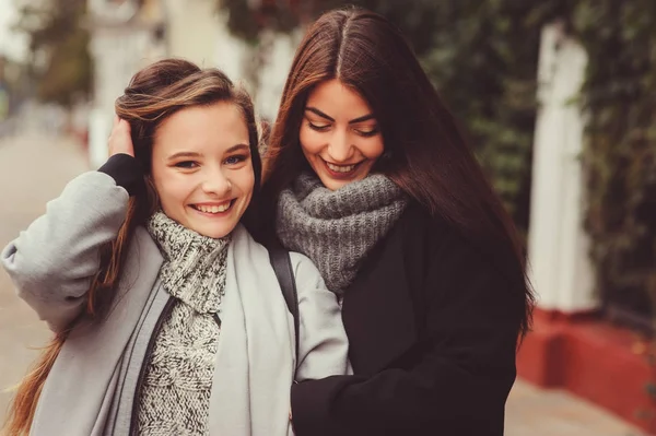 Zwei junge, glückliche Freundinnen, die in lässigen Outfits durch die Straßen der Stadt laufen, warme Mäntel tragen und Spaß haben — Stockfoto