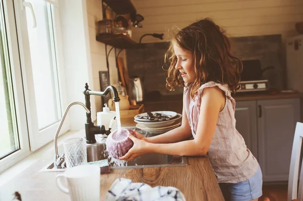 Niña ayuda a la madre en casa y lavar los platos en la cocina. Estilo de vida casual en el interior real. Enseñar a los niños a hacer el trabajo doméstico . — Foto de Stock