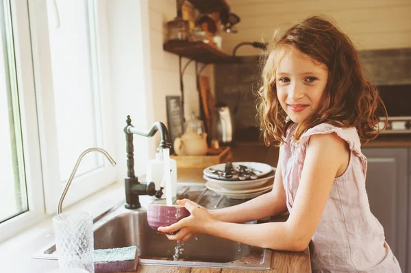Niña ayuda a la madre en casa y lavar los platos en la cocina. Estilo de vida casual en el interior real. Enseñar a los niños a hacer el trabajo doméstico . — Foto de Stock
