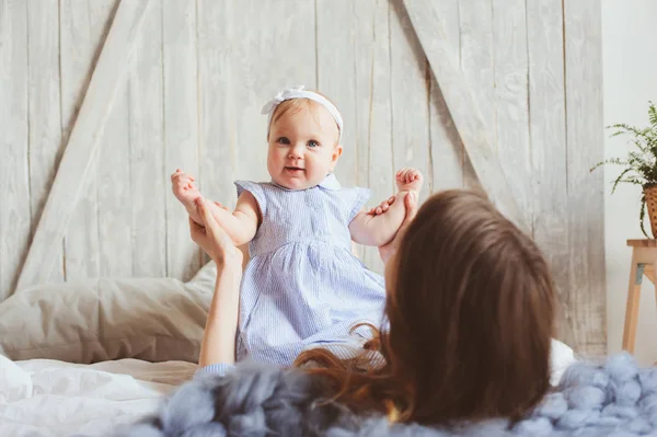 Gelukkig moeder en 9 maand oude baby in bijpassende pyjama's spelen in slaapkamer in de ochtend. Gezellig familieweekend. — Stockfoto