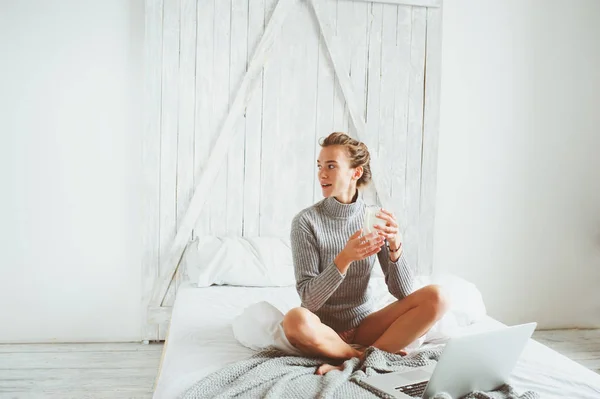 Молода блогерка або ділова жінка, яка працює вдома з соціальними медіа, п'є каву вранці в ліжку. Сучасне життя в скандинавському інтер'єрі, побутовий спосіб життя — стокове фото