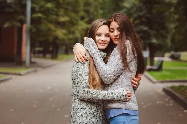 Zwei junge, glückliche Freundinnen, die in lässigen Outfits durch die Straßen der Stadt laufen, warme Pullover tragen und Spaß haben — Stockfoto