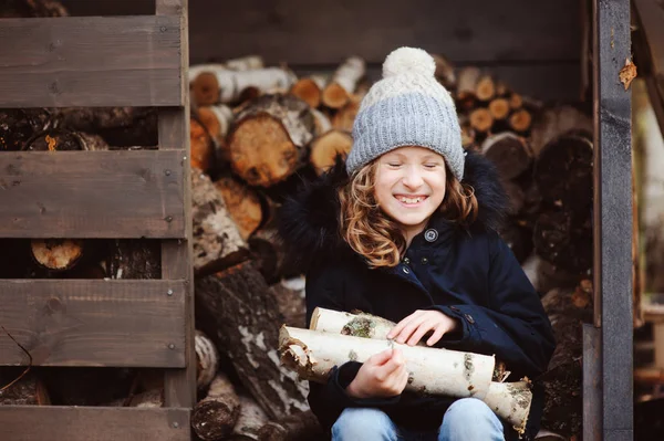 Happy child girl picking firewood from shed in winter or autumn — Stock Photo, Image