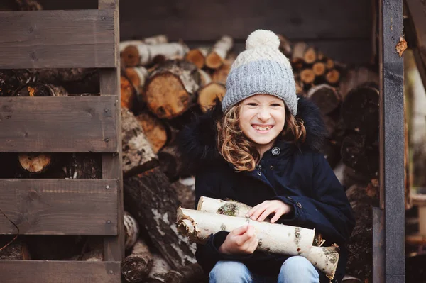 Bambino felice ragazza raccogliere legna da ardere da capannone in inverno o in autunno — Foto Stock