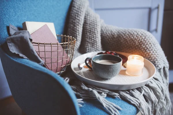 Cozy winter weekend at home. Morning with coffee or cocoa, books, warm knitted blanket and nordic style chair. Hygge concept.