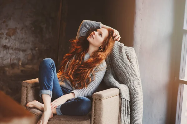 自宅カジュアル セーターとジーンズを着て 居心地のよい椅子でリラックス若いリードヘッドの女性 穏やかな冬や秋の週末 — ストック写真