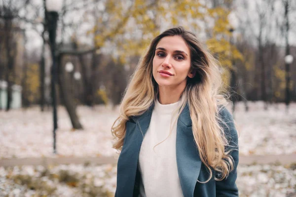 winter portrait of young woman walking in snowy city park in warm grey coat