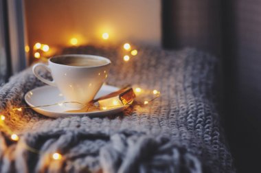 Kış veya sonbahar sabahı evde rahat. Sıcak kahve altın metal kaşık, sıcak battaniye, garland ve mum ışıkları, İsveçli hygge kavramı ile.