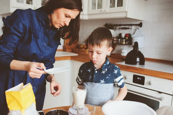 Kid boy helps mother to cook in modern white kitchen. Happy family in cozy weekend morning at home