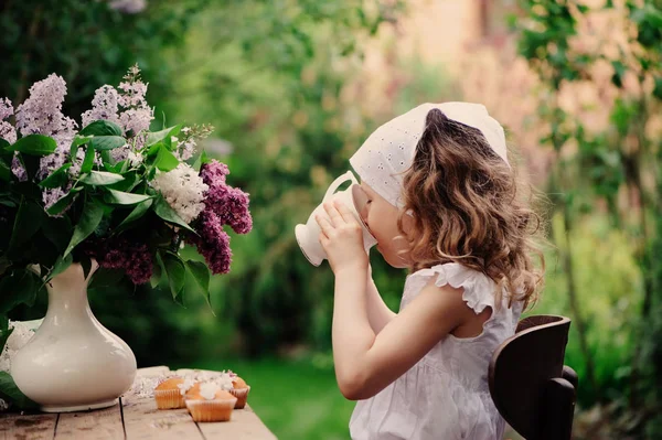 女孩在庭院茶党在春天天与花束丁香 质朴的木桌和复古礼服 — 图库照片