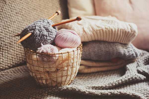 Grey and pink Yarn ball with knitting needles in metallic basket with knitted sweaters on background. Hobby, cozy homely weekend and hugge concept.