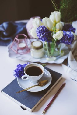 fincan kahve, kitap ve beyaz masaya çiçek bahar sabah evde. Mevsimlik dekorasyon, rahat yaşam, hygge kavramı
