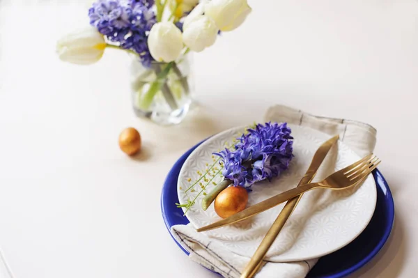ゴールデンで金属刃物と卵 ヒヤシンス チューリップの花束 青と白プレートとイースター ホリデー ダイニング テーブル お祝いのコンセプト — ストック写真