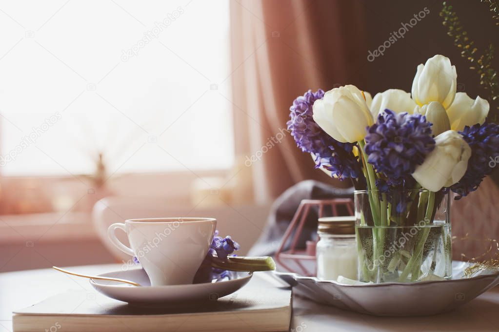 spring morning at home with cup of coffee, book and flowers on white table. Seasonal decoration, cozy living, hygge concept