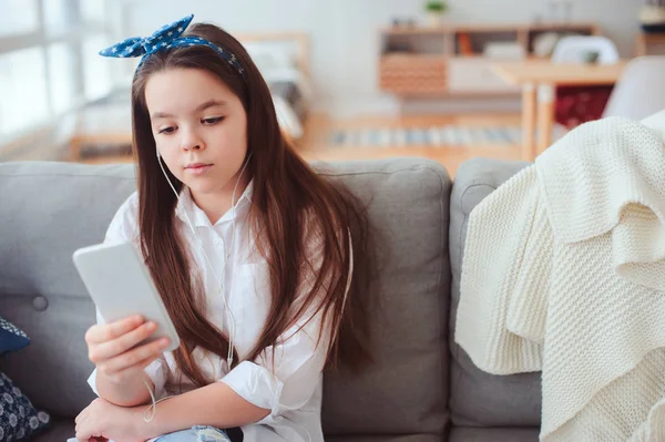 快乐的青春期女孩在家放松舒适的沙发和听音乐 使用智能手机 — 图库照片