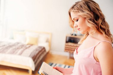 trendy bahar etek ve üst giyen genç güzel kadın kitap okumak evde rahat hafta sonu sabah.