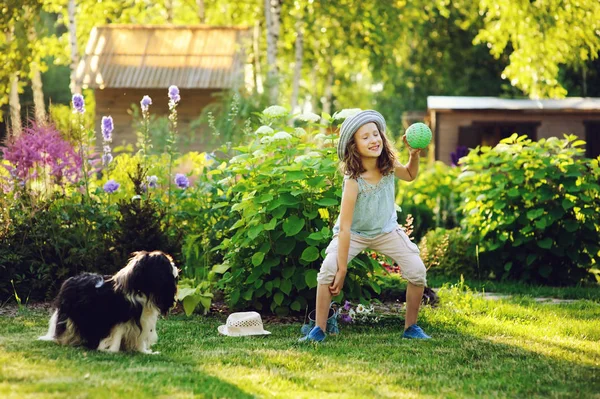 庭の日当たりの良い夏の日を楽しんで幸せな子供女の子彼女のスパニエル犬と遊ぶと ボールを投げる — ストック写真
