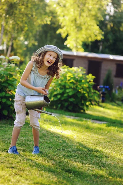 幸福的女孩的垂直的画像在园丁帽子玩浇水罐头在阳光明媚的夏日花园 — 图库照片