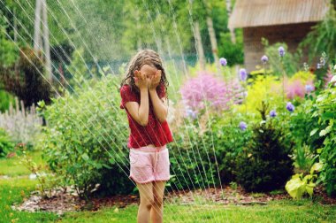 Bahçe yağmurlama ile sıcak yaz günde oynayan kız evlat. Çocuklar için su açık hava etkinlikleri mutlu çocukluk.