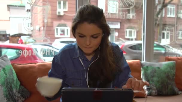 An angry Caucasian girl woman surfing on a tablet In Cafe and drinking coffee — Stock Video