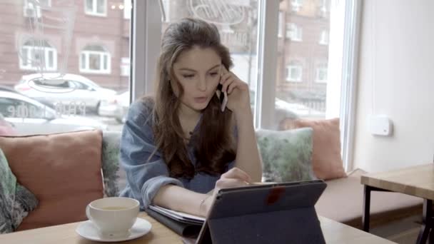 Jonge Kaukasische zakenvrouw spreekt via telefoon en surfen op een tablet in Cafe — Stockvideo