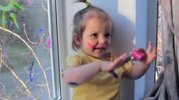 Glad liten flicka med färg på händerna nära fönstret. Grabben på hemmaplan. Karantän — Stockvideo