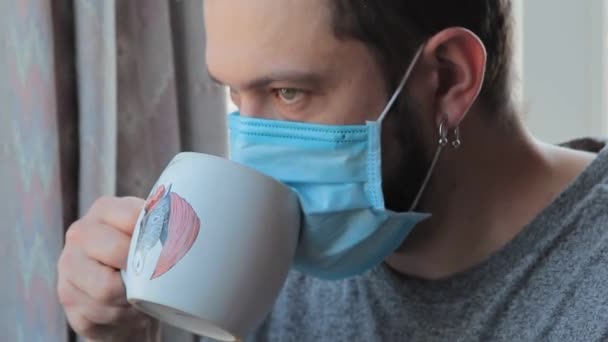 Coronavirus fun. Funny Man at home drinking tea through protective mask. Crazy at home Male in quarantine. Close-up — Stock Video