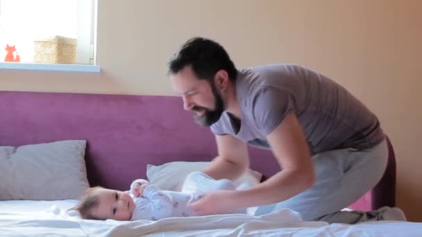 Młody ojciec zmienia pieluchę i ubrania dla dziewczynki w domu — Wideo stockowe