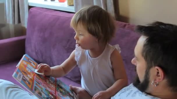 Far läser en bok med sin lilla dotter hemma. — Stockvideo