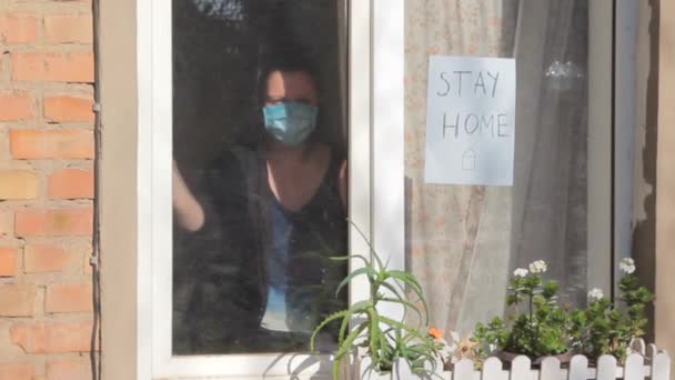 Självisolering, coronavirusepidemi. Kvinnan i skyddsmask drar ridån. Stanna hemma och var trygg. — Stockvideo