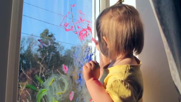 Ένα κοριτσάκι ζωγραφίζει στο παράθυρο. Το παιδί στο σπίτι. Καραντίνα — Αρχείο Βίντεο