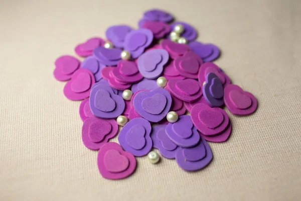 Фіолетові серця і перлини лежать на бежевій тканині — стокове фото