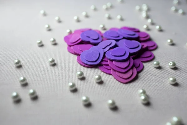 Фіолетові серця і перлини лежать на бежевій тканині — стокове фото