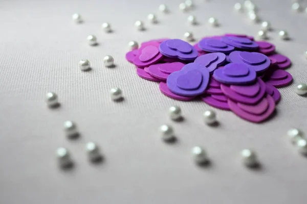Purple hearts and pearls lying on a beige fabric — Stock Photo, Image